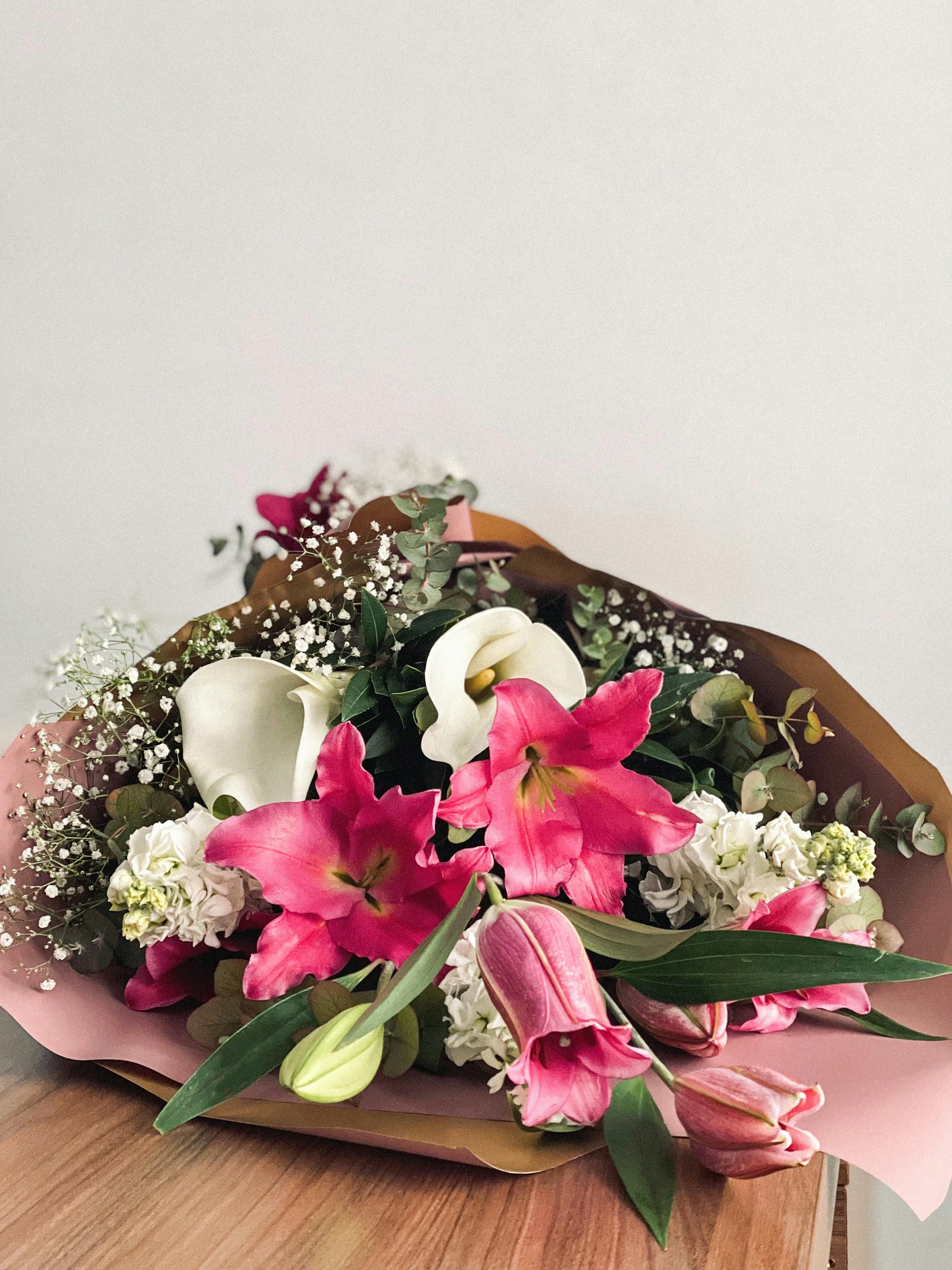 A beautiful bouquet featuring pink lilies, calla lilies, and baby's breath on a table.